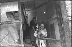 Child holds the flimsy boards that remain of the door to an apartment house