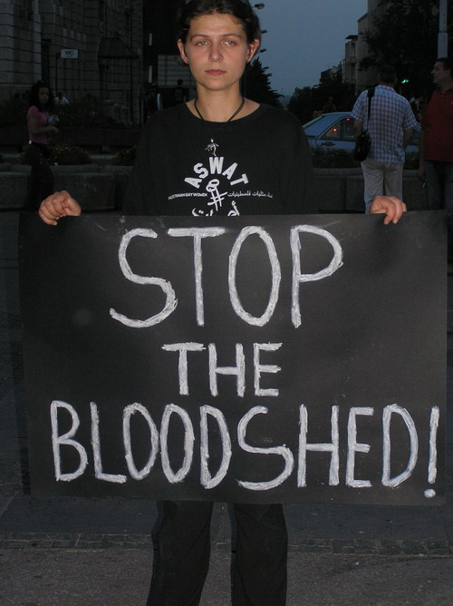 Woman wearing ASWAT T-shirt while holding sign that says Stop the Bloodshed