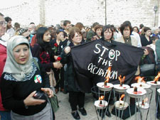 Luisa Morgantini, Zahira Kamal and others stand by the torches while holding a banner saying 'STOP THE OCCUPATION'