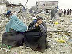 Two women sit weeping in the field of rubble where their homes used to be 