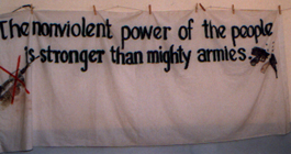 Clothespins on a string hold a large cloth banner which says 'The nonviolent power of the people is stronger than mighty armies.'