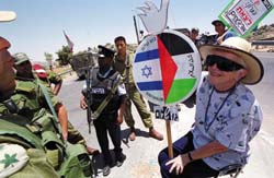 Dalia Pilavsky holds a sign displaying the Israeli and Palestinian flags topped by a dove as she faces an Israeli soldier