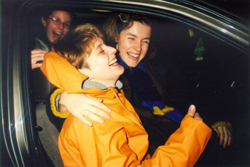 Three lesbians laughing uproariously in a car, the one in the foreground wearing a bright yellow slicker